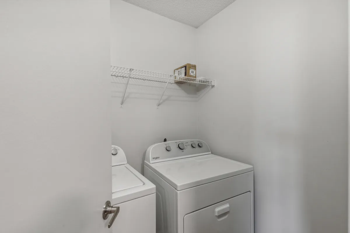 The image showcases an in-unit laundry area with a washing machine, dryer, and shelf for organizing laundry supplies. The space is practical, tidy, and emphasizes convenience for personal laundry needs.