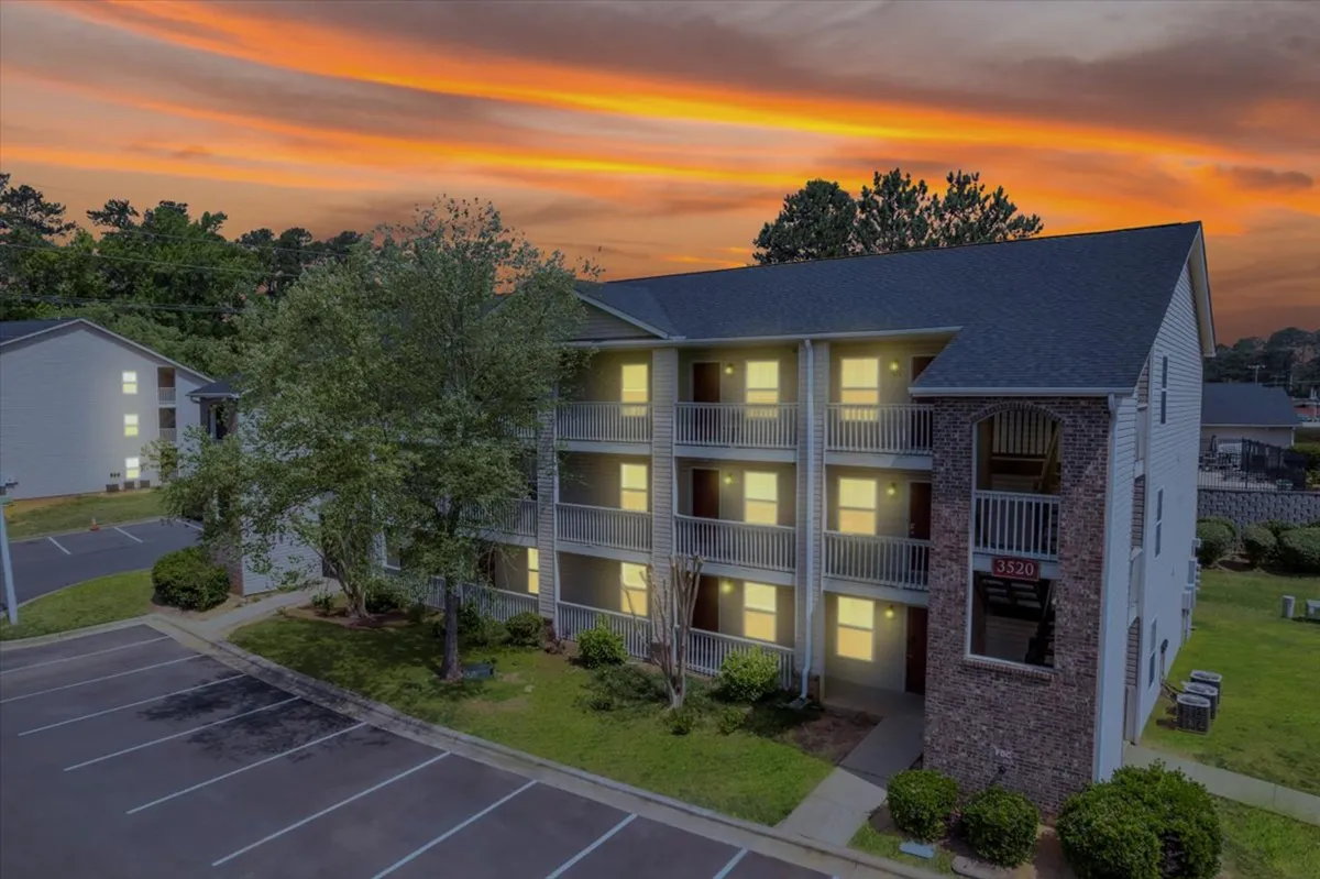 A three-story building with balconies, surrounded by greenery and set against a sunset sky. The image conveys a peaceful, welcoming environment, with the potential for relaxing on balconies and enjoying the outdoors.