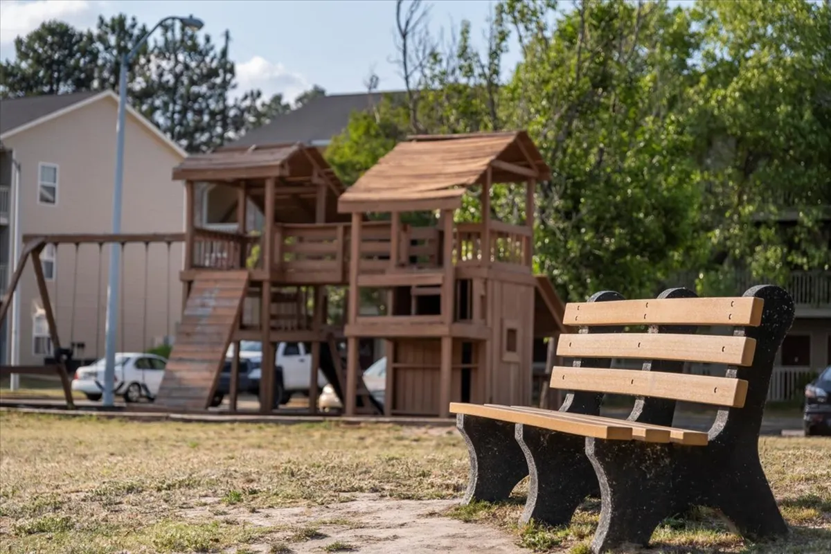 An inviting exterior scene featuring a well-maintained playground and a nearby bench set in a green space. The setting is bright and open, encouraging outdoor exploration and relaxation.