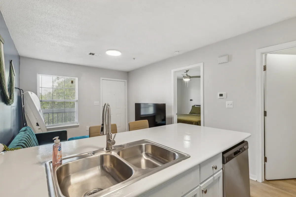 A welcoming interior view of a modern, open living area featuring a kitchen island, cozy living space with television, and a door leading to the bedroom. The layout is spacious and conducive to relaxing or spending intimate evenings in.
